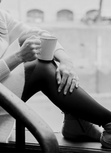 Person sitting on a window sill with a cup. The focus is on the shoes.