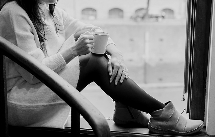 Person sitting on a window sill with a cup. The focus is on the shoes.