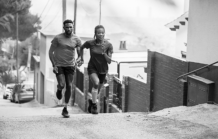 Two people running up a hill with sports clothes.